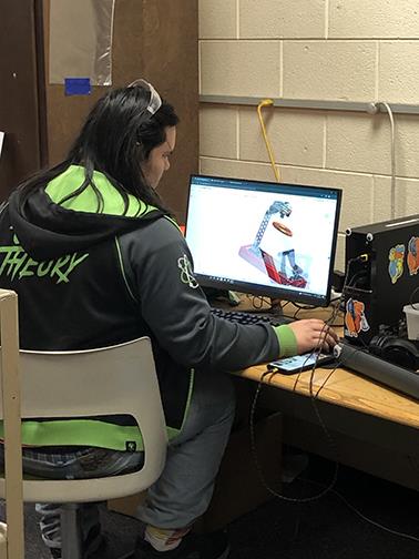 Student sitting at computer with CAD drawing.